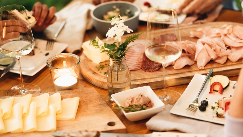 Ein gedeckter Tisch mit Brot, Käse, Aufschnitt und Weingläsern.