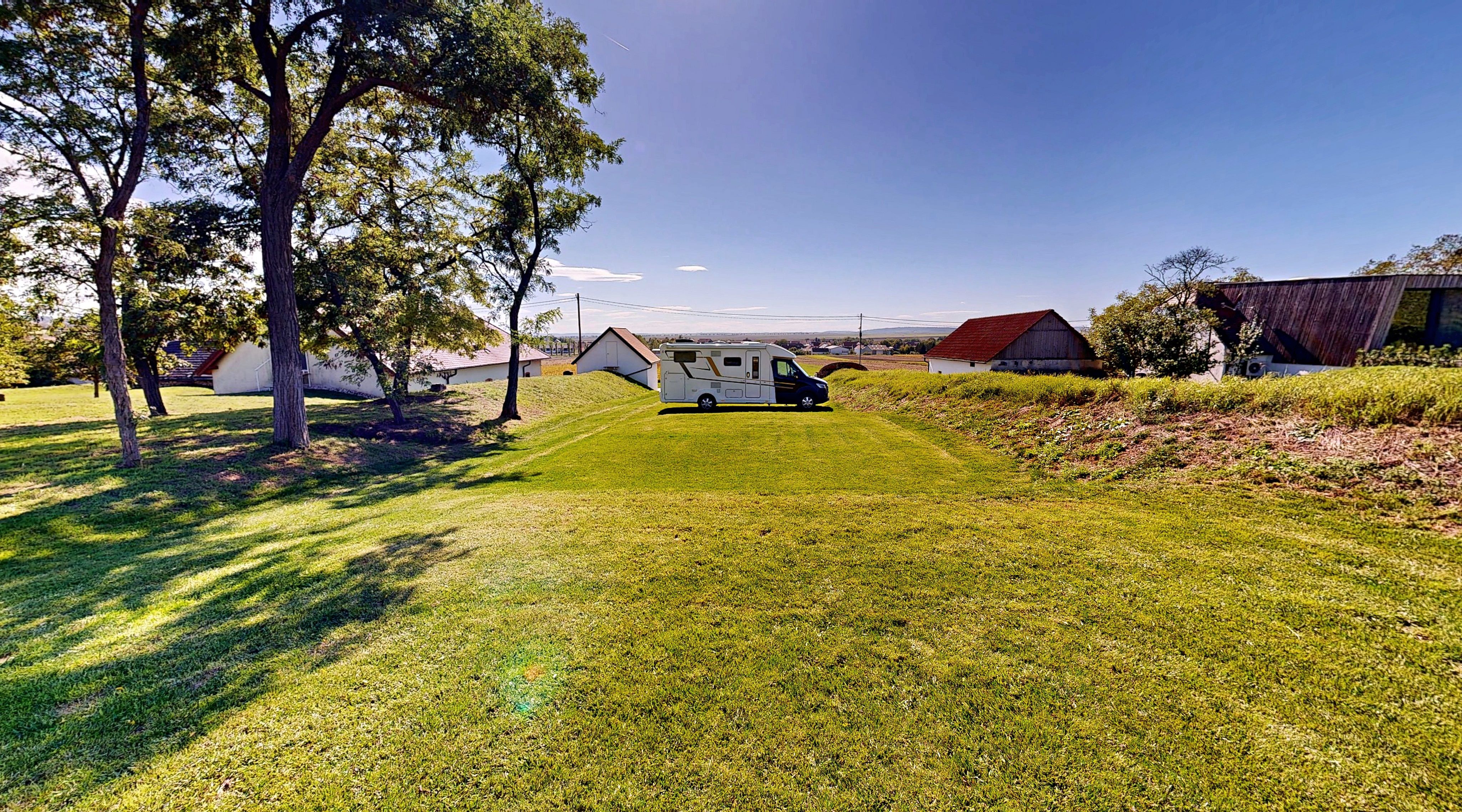 Wohnmobil auf einem grünen Campingplatz mit Bäumen und Gebäuden im Hintergrund.