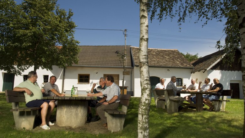 Menschen sitzen an Tischen im Freien vor traditionellen Gebäuden in Schöngrabern.