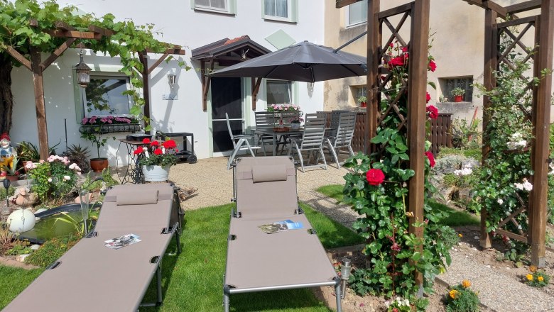 Garten mit Liegestühlen, Pergola und Blumen.