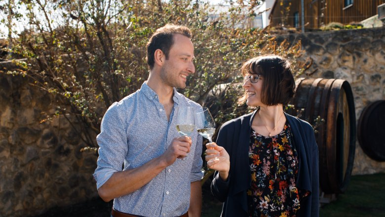 A man and a woman clink glasses of wine outside.