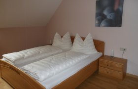 Ein schlichtes Gästezimmer mit einem Doppelbett, weißen Bettdecken und einem Nachttisch mit Lampe.