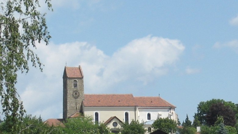 Kirche mit Turm und rotem Dach in Hohenwarth, umgeben von Bäumen und blauem Himmel.