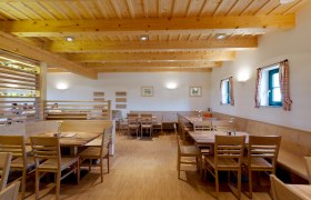 Innenansicht eines gemütlichen Gastraums mit Holzmöbeln und Holzbalkendecke.