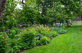 Ein Bauerngarten mit üppiger Vegetation, bunten Blumen und einem gepflegten Rasen.