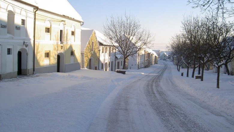 Verschneite Straße mit historischen Gebäuden und Bäumen in Straning, Österreich.