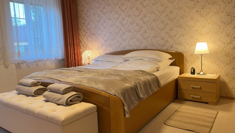 Gemütliches Schlafzimmer mit Doppelbett, Nachttischlampe und Fenster mit Vorhängen.