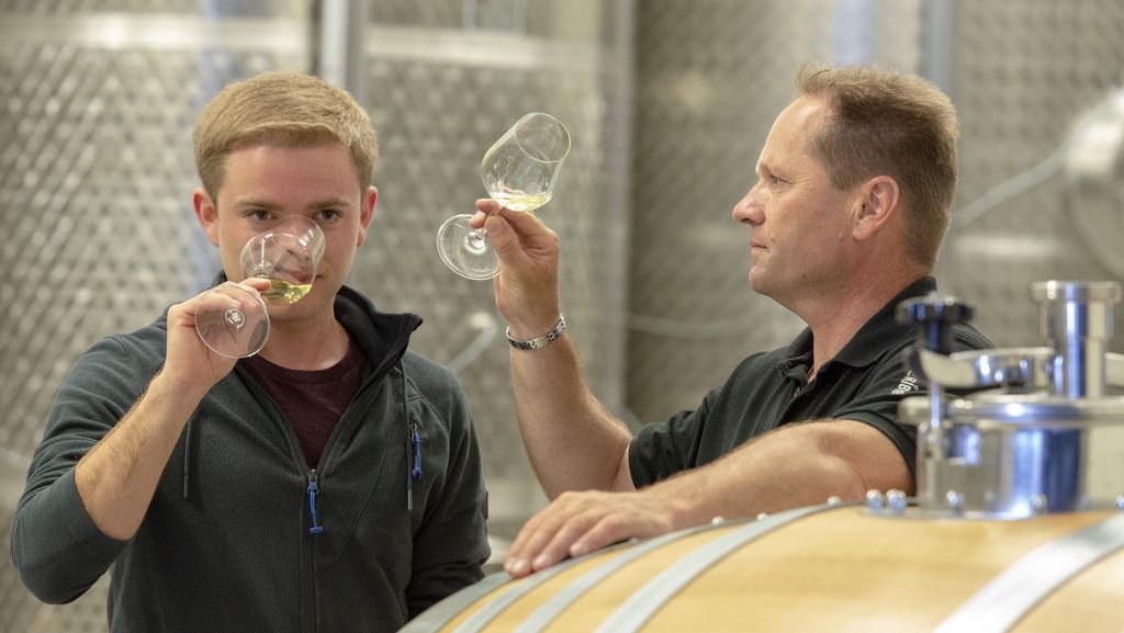 Two men tasting wine in a wine cellar.