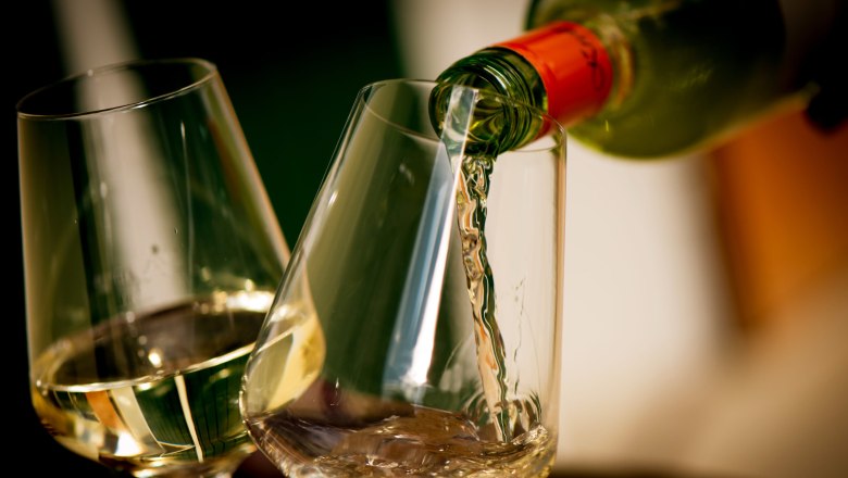 Wei&szlig;wein wird in ein Glas eingeschenkt, daneben ein weiteres gef&uuml;lltes Glas.