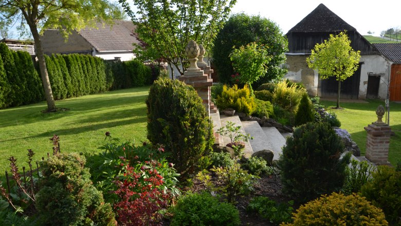 Ein gepflegter Garten mit Rasen, Büschen und Bäumen, umgeben von Gebäuden im Hintergrund.