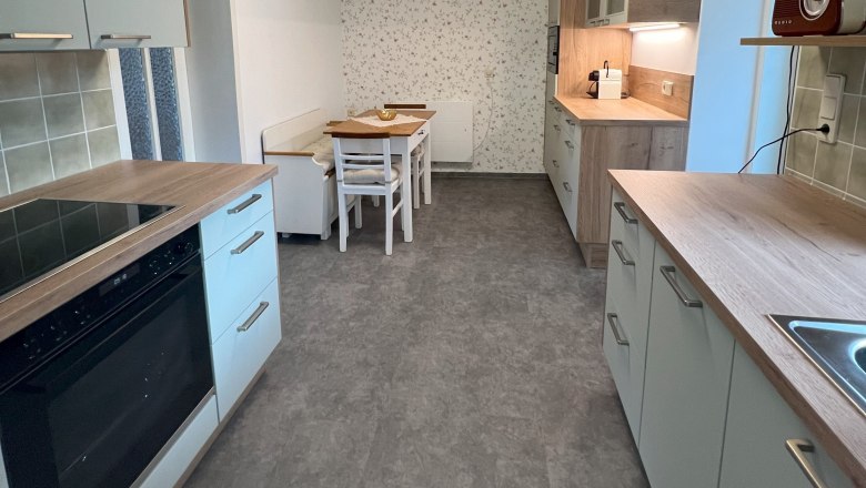 Moderne Küche mit grauen Schränken, Holzakzenten und einem Esstisch. An der Decke eine geometrische Lampe.