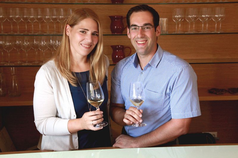 A smiling couple holding wine glasses in a wine cellar.