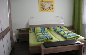 Gästezimmer mit Doppelbett, bunter Bettwäsche und Wandbild.