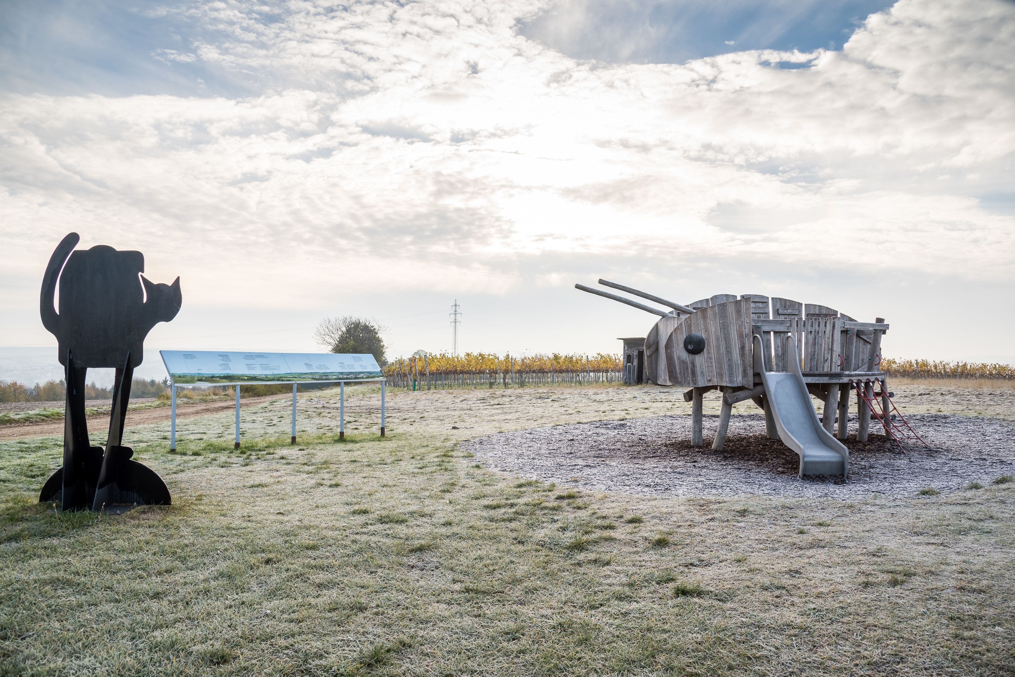 Spielplatz mit Holzspielgerät in Form eines Tieres und Katzenskulptur.