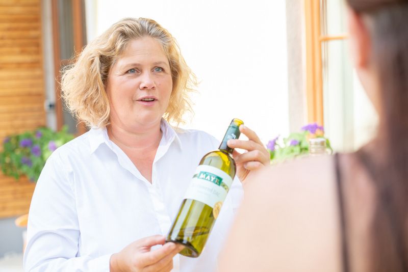 A woman holds a bottle of wine and talks to another person.