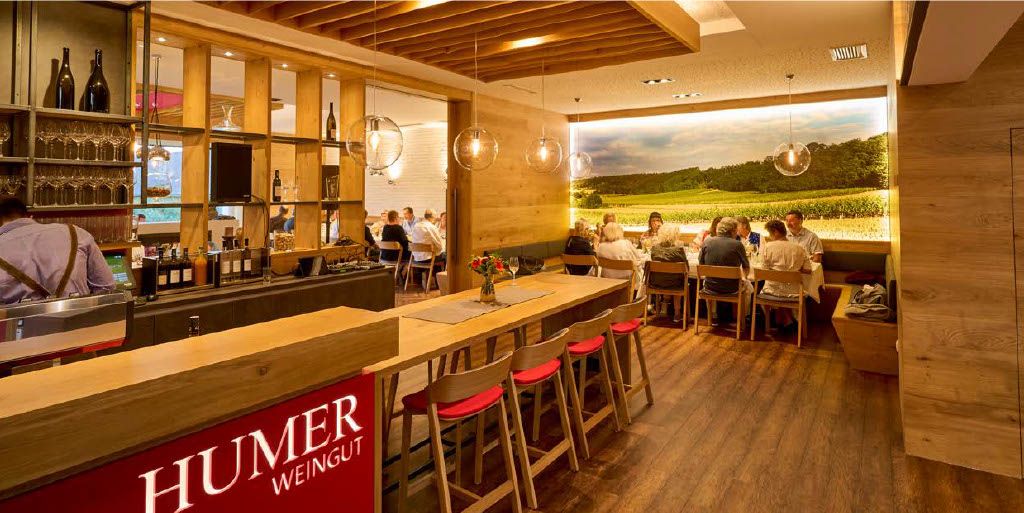 Innenansicht eines modernen Heurigenlokals mit Holzmöbeln und einer großen Fototapete eines Weinbergs.