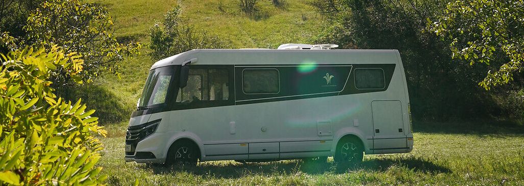 Umgeben von üppigem Grün und unter einem strahlend blauen Himmel, bietet der Campingwagen einen perfekten Rückzugsort für Naturliebhaber. Die sanften Hügel im Hintergrund und die historische Burgruine schaffen eine malerische Kulisse, die zum Entspannen und Erkunden einlädt.