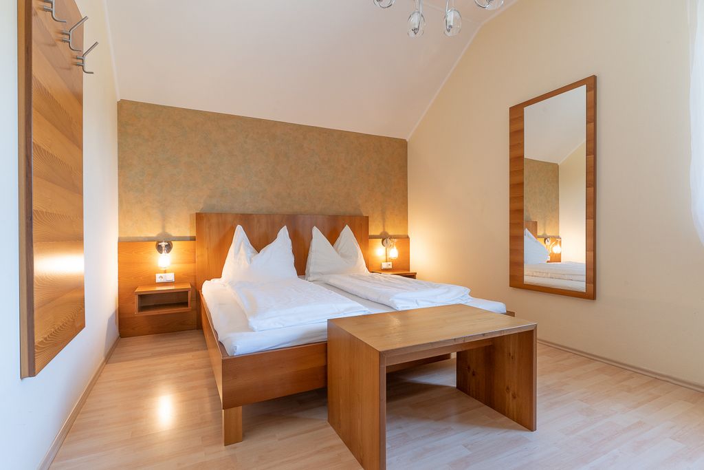 Gemütliches Schlafzimmer mit Doppelbett, Holzmöbeln und großem Spiegel.