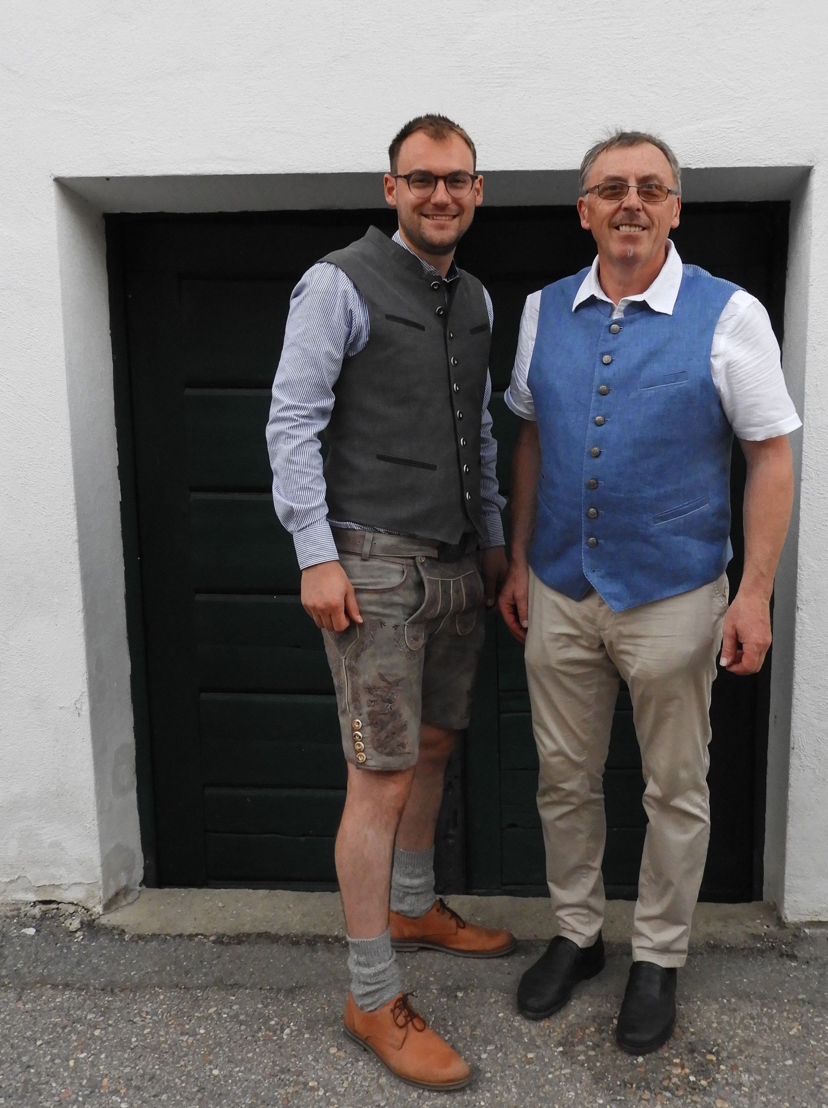 Two men in traditional dress in front of a dark door.