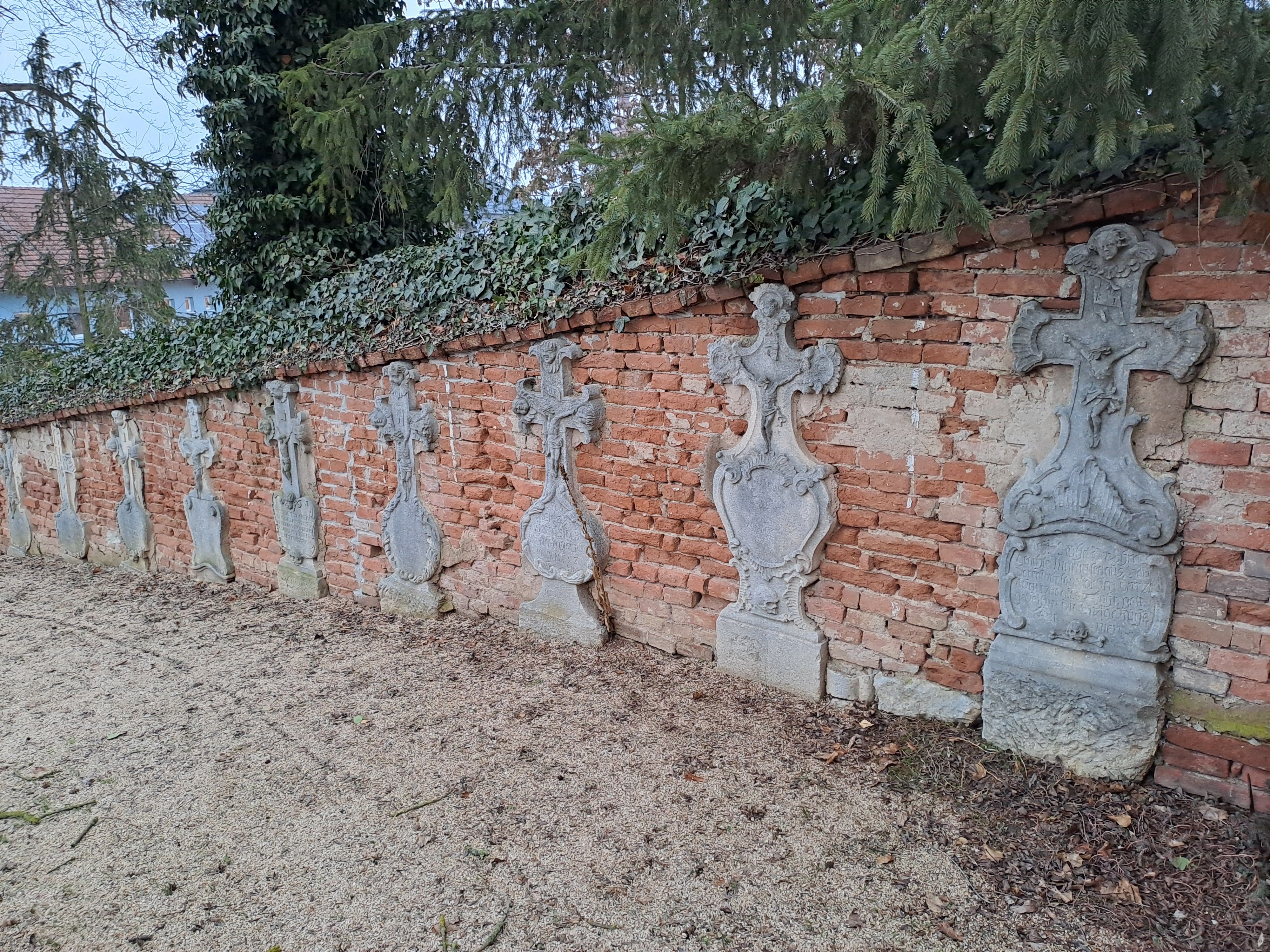 Row of sandstone crosses in front of a brick wall in Ravelsbach.