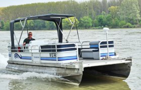 Ein kleines Motorboot fährt auf einem Fluss, umgeben von Bäumen am Ufer.