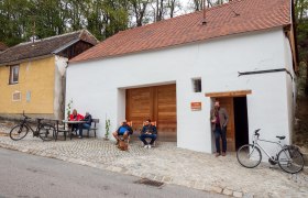 Menschen sitzen vor einem Kellergebäude mit Fahrrädern.