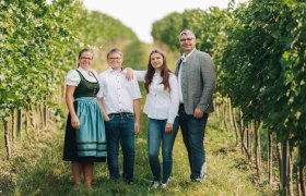 Eine Familie steht lächelnd in einem Weinberg.