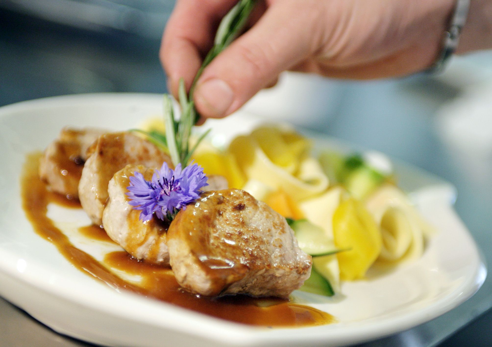 A plate with meat, sauce, pasta and vegetables, decorated with a flower and rosemary.