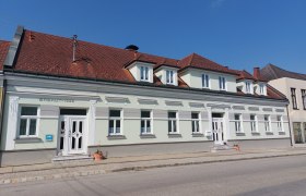 Ein zweistöckiges Gebäude mit rotem Ziegeldach und weißen Fensterrahmen, erbaut 1922, bei sonnigem Wetter.
