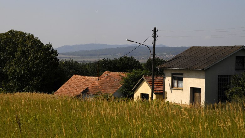 Ländliche Szene mit Häusern und Wiesen im Vordergrund, Hügel im Hintergrund.