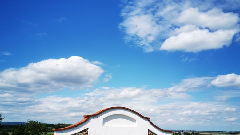 Kleines Steinhaus in einem Weinberg unter blauem Himmel mit Wolken.