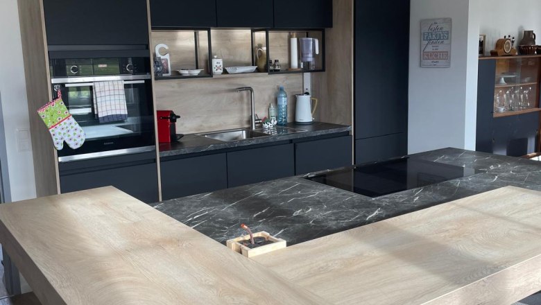 Moderne Küche mit Holz- und Marmorelementen, drei Hängelampen und schwarzen Schränken.