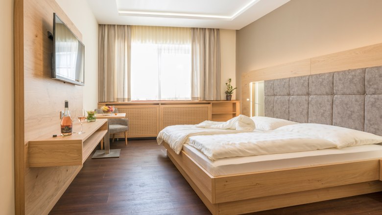 Modernes Gästezimmer mit Doppelbett, Flachbildfernseher und Holzmöbeln.