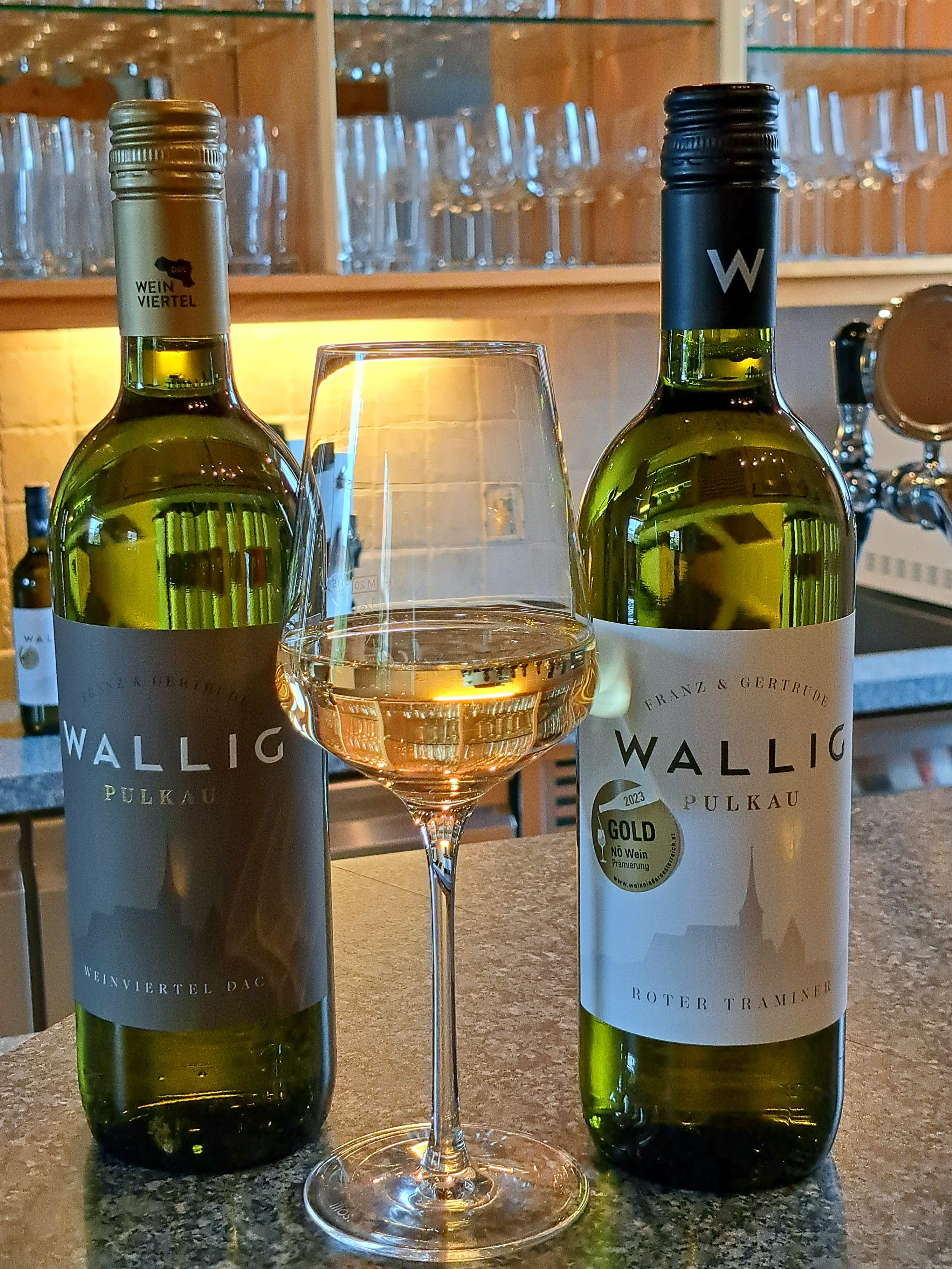 Zwei Weinflaschen und ein Glas Weißwein auf einer Theke.