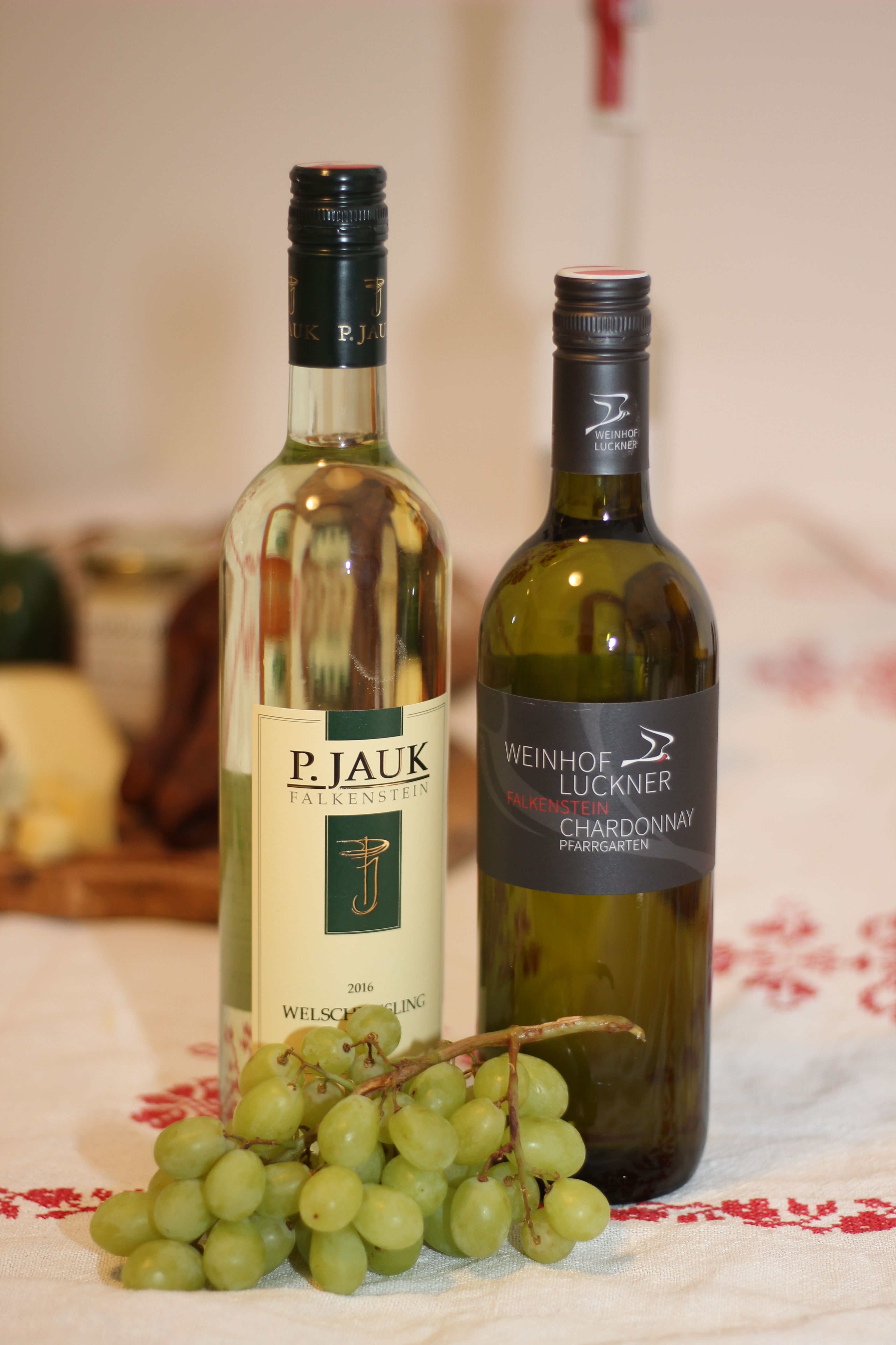 Zwei Weinflaschen und ein Bund grüner Trauben auf einem Tisch.