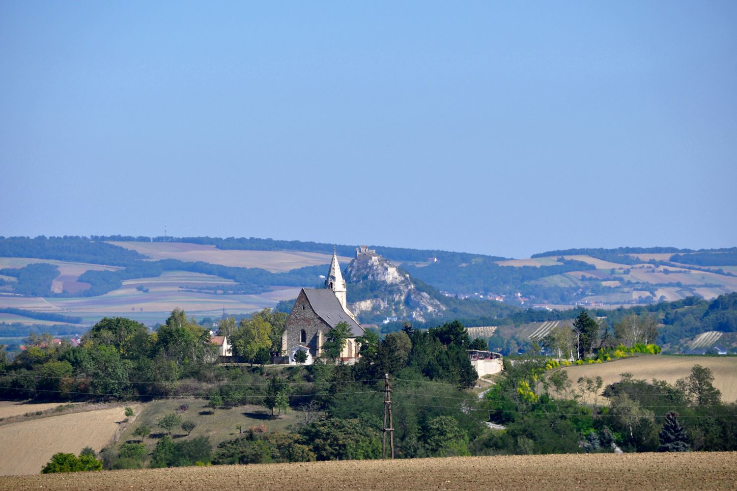 Landschaft mit Kirche und Hügel im Hintergrund.