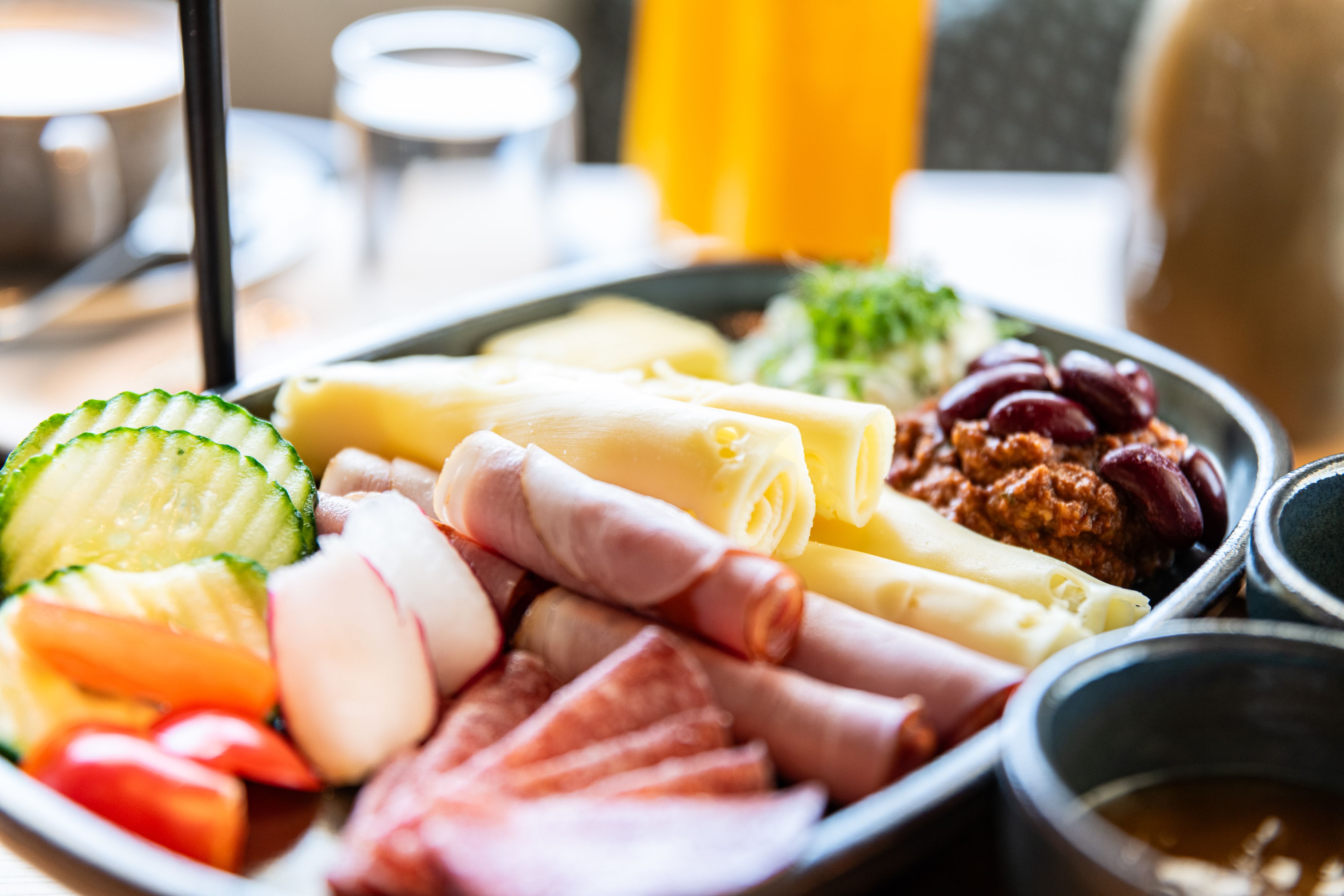 Nahaufnahme eines Frühstückstellers mit Käse, Schinken, Salami, Gemüse und Bohnen.