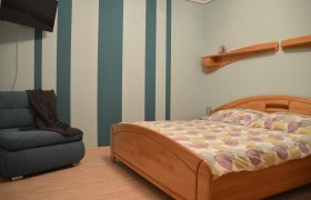 Schlafzimmer mit gestreifter Wand, Holzbett und Sofa.