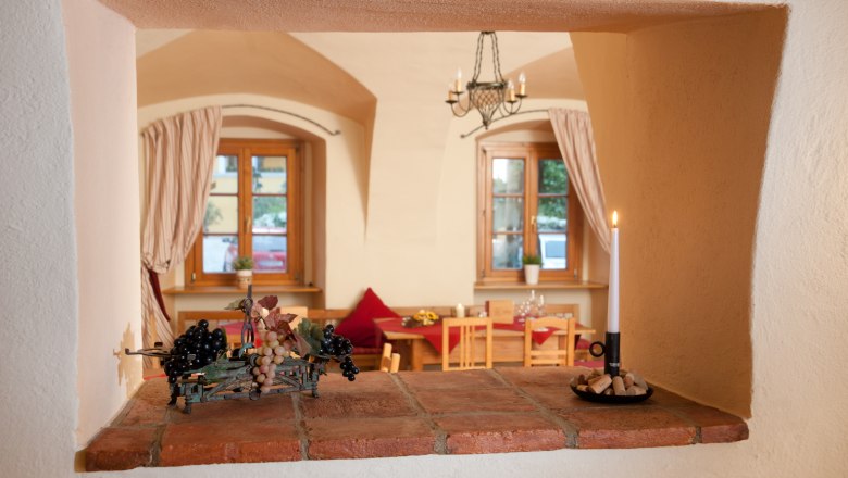 Blick durch eine Maueröffnung in einen gemütlichen Raum mit Holzmöbeln und Kerzenlicht.