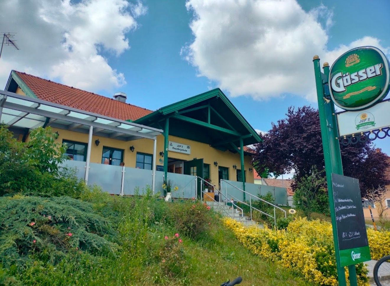 Gelbes Gasthaus mit Büschen und Blumen im Vordergrund
