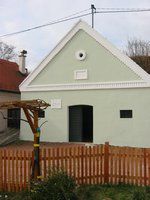 Malá, světle zelená budova se šikmou střechou a dřevěným plotem před ní.