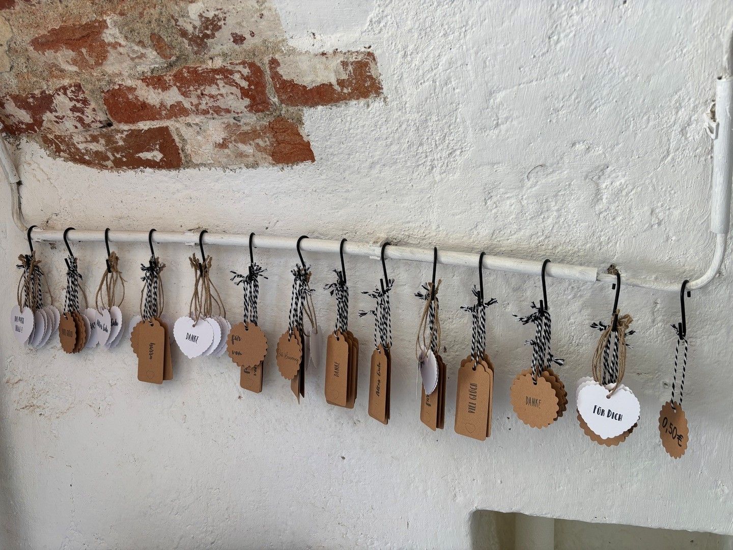 An einer weißen Wand hängen an einer Leiste viele kleine Anhänger mit Dankes- und Preisaufschriften, vermutlich an der Trinkstation von Weinbau Ackerl.