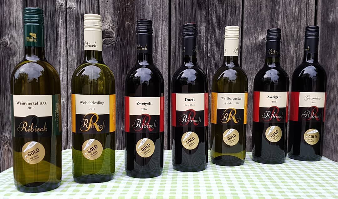 Seven bottles of Ribisch wine on a table in front of a wooden wall.