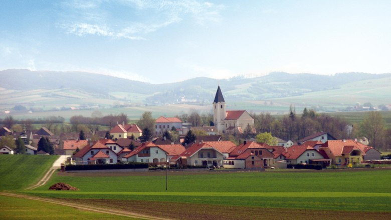 Panorama von Großharras mit Kirche und Hügeln im Hintergrund.