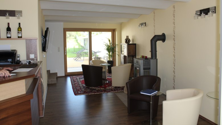 Innenansicht eines modernen Gästehauses mit Sitzbereich, Kamin und Glastür zum Garten.