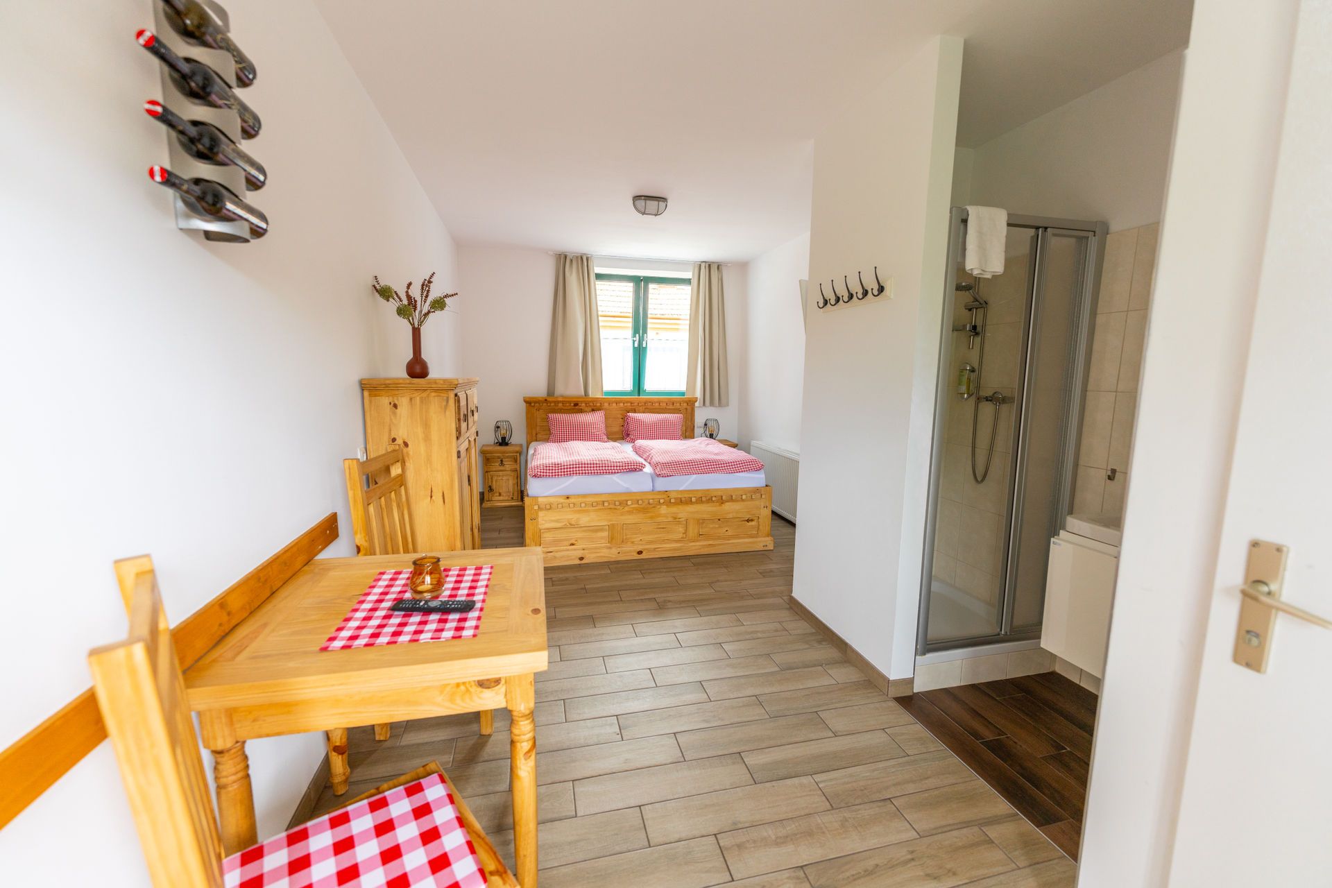 Zimmer im Winzerhof Küssler mit Doppelbett, kleinem Tisch, Bad mit Dusche und Weinflaschen-Deko an der Wand.