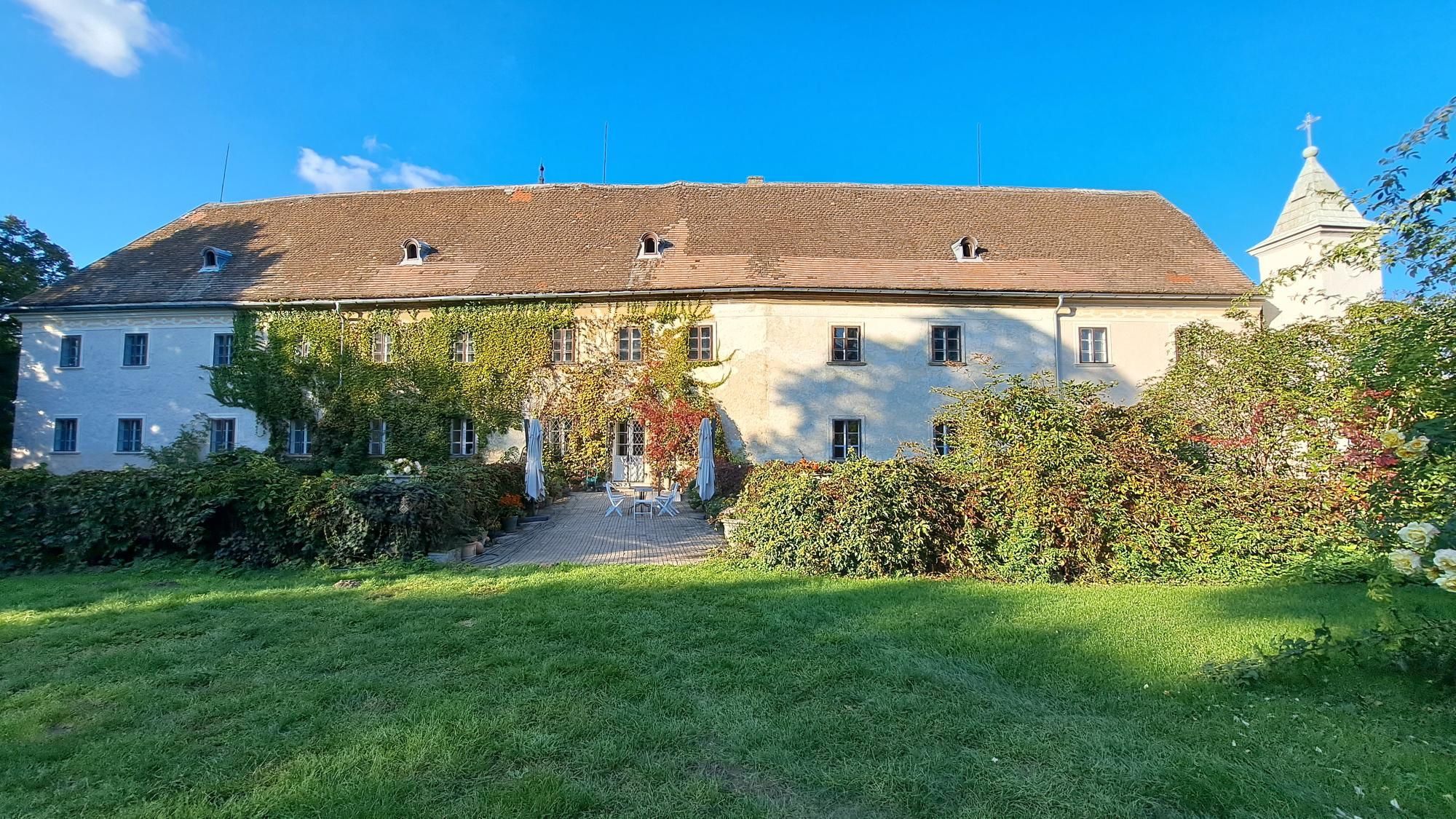 Schloss Poysbrunn mit bewachsener Fassade und Garten.