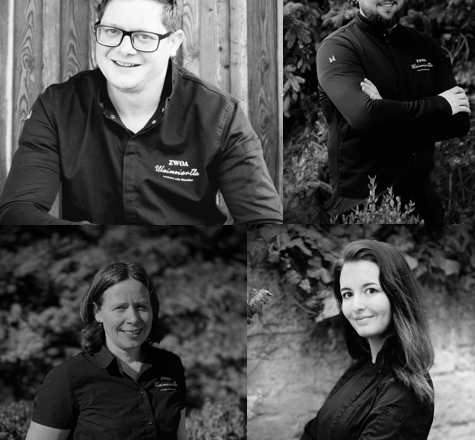 Vier Personen in Schwarz-Weiß-Porträts, die lächeln und in Arbeitskleidung posieren.