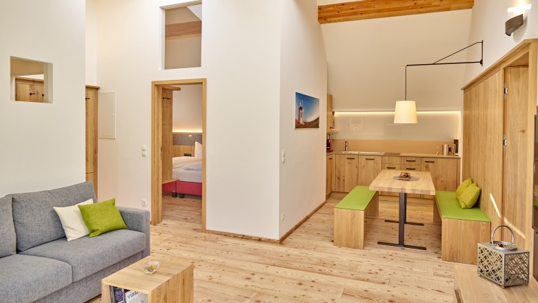 Modernes Wohnzimmer mit Holzmöbeln, grauem Sofa und offener Küche.