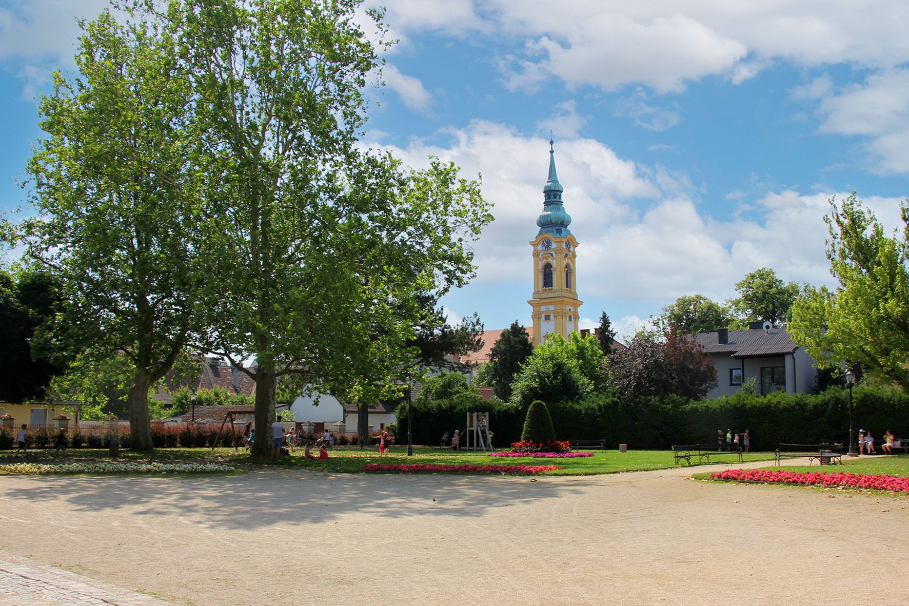 Ein Park mit Blumenbeeten, Bäumen und einem Kirchturm im Hintergrund.